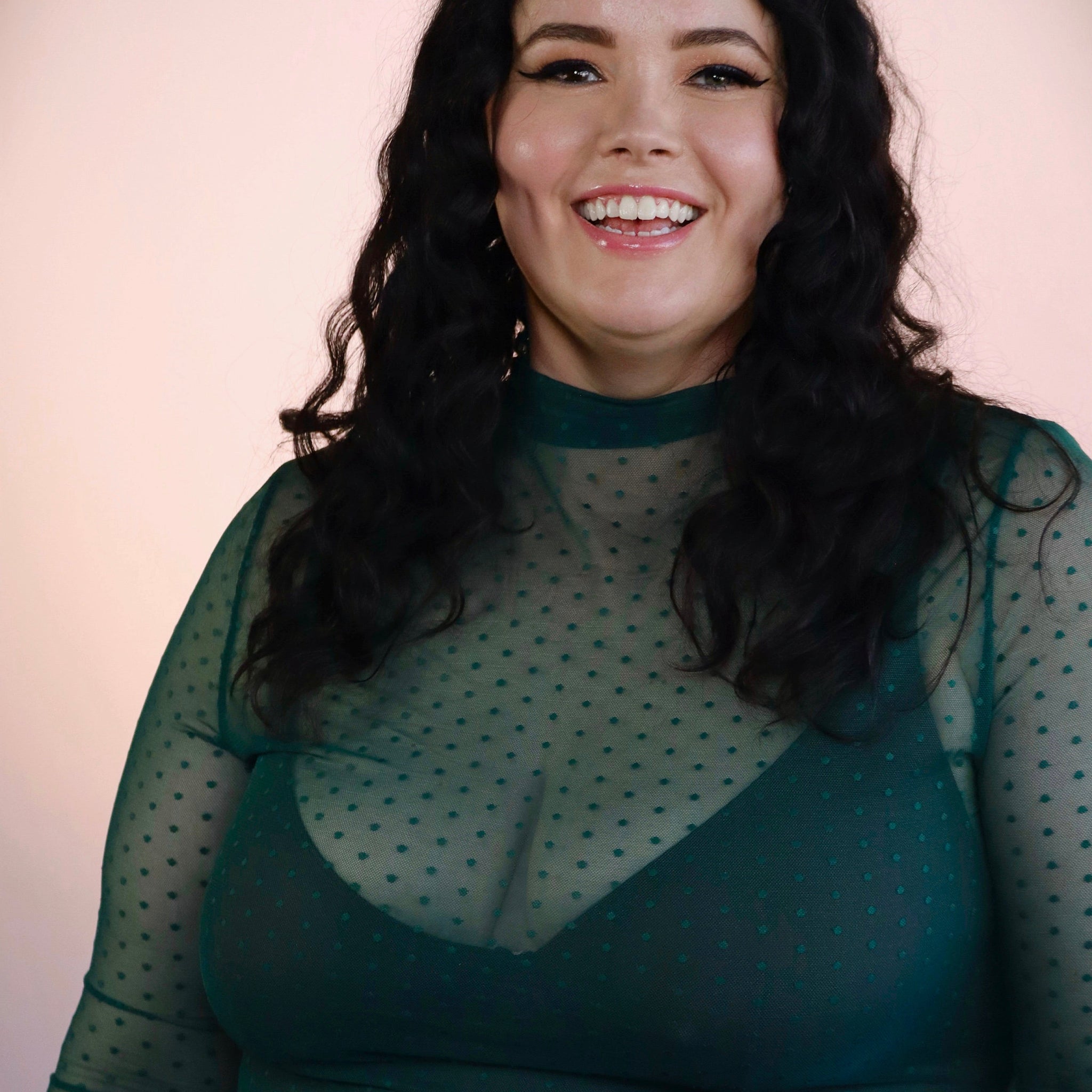 Woman wearing a green sheer top with a plain background
