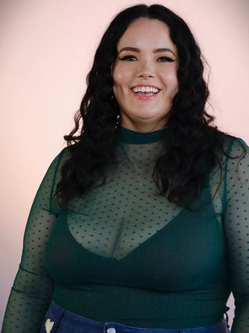 Woman wearing a green sheer top with a plain background